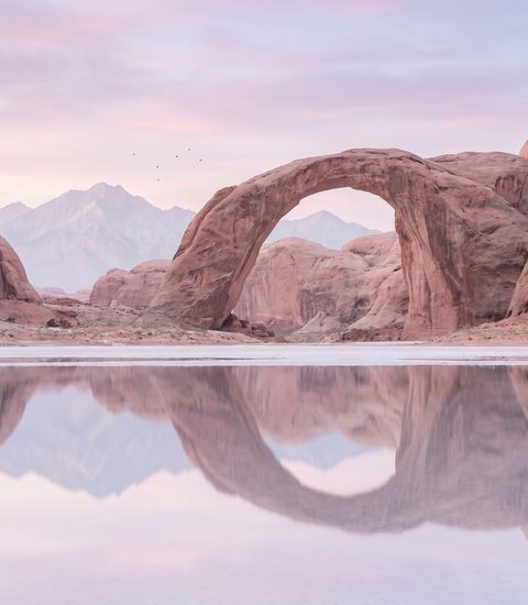 A stone arch above a mirror-flat desert lake